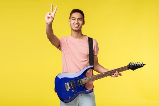 Lifestyle, leisure and youth concept. Peace my friends. Portrait of enthusiastic handsome asian guy playing on stage, performing song, holding electric guitar, invite listen to his band