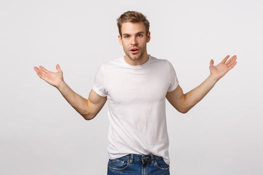 What you want. Confused and careless handsome blond caucasian guy spread hands sideways questioned, shrugging asking question, cant understand, dont know, standing indecisive