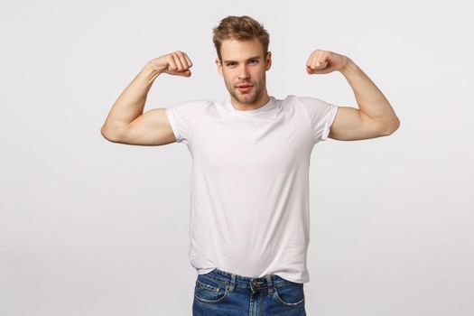 Masculine confident and sassy blond bearded caucasian man, standing white background with flexed biceps, be in good shape, workout and bragging, being boastful own body shape or strength