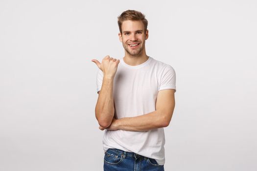 You should see this. Carefree, casual handsome blond caucasian bearded guy, pointing thumb left and smiling during conversation talking about company, product or banner, indicate where find