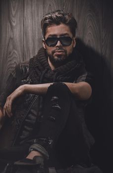relaxed fashion man in sunglasses sits on wood in studio