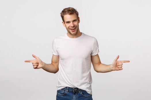 Have a look at this two. Attractive sassy macho man with bristle, blond hair, suggest choices, pointing sideways, indicate left and right banners with products and smiling pleased, white background