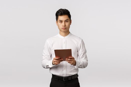 Business, finance and recruitment concept. Handsome elegant young asian man holding digital tablet and looking camera serious, being busy, control work remote, hr interviewing applicants