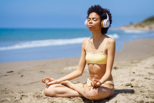 Black girl in lotus pose doing mindfulness listening to a meditation with wireless headphones.