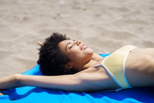 Smiling black woman lying on the sand of a tropical beach sunbathing
