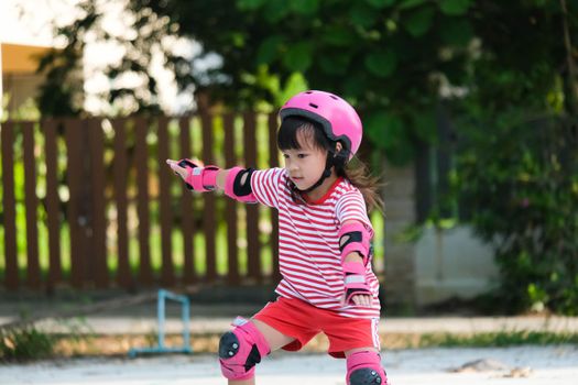 Cute Asian little girl in protective pads and safety helmet practicing roller skating in the park. Exciting outdoor activities for kids.