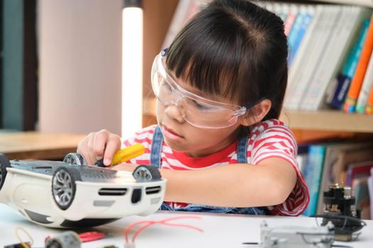 Concentrated little girl repairing her toy car with a tool in hand and carefully assembles toy car with screwdriver. STEM Hobbies for advanced smart kids.