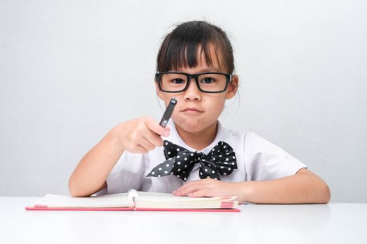 Cute Asian little girl plays teacher role game or little businesswoman taking notes while working in the office. Homeschool children's play and learning.