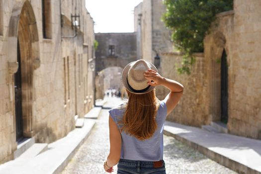 Tourism in Rhodes, Greece. Back view of traveler girl goes down the Street of the Knights of Rhodes city, Greece. Young female traveler visiting southern Europe.