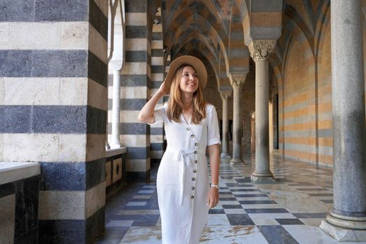 Beautiful young tourist woman looks to the side when walks in the colonnade outside the Saint Andrew Cathedral of Amalfi, Italy