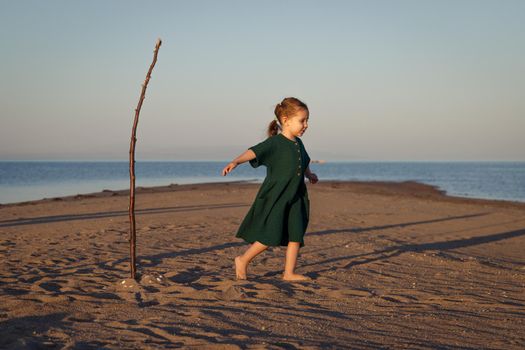 Cute little girl in green dress playing on the beach in a desert island