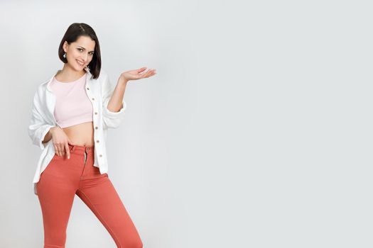 Cute brunette woman 30s in coral jeans, pink tank top and white shirt on white background. High key vertical shot