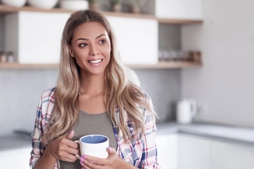 cute young woman with mug standing in kitchen