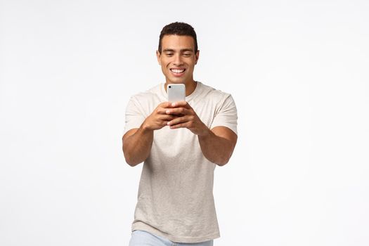 Cheerful, excited good-looking brazilian man with strong muscles, holding smartphone, looking enthusiastic gadget screen, record video, attend amusing event, taking photos on telephone camera