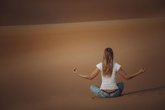 Back Side of Young Female Doing Yoga Exercises in the Desert. Meditation on Beautiful Peaceful Sandy Background. Soul Balance and Harmony Concept.