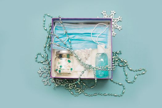 Medical mask, pills in a jar, antiseptic gel for hands and Christmas decorations in a box on a blue background. Christmas gifts in the age of coronavirus.