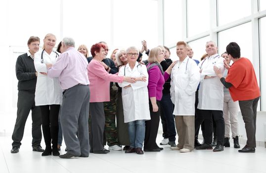 Group of seniors and doctors hugging indoors full length