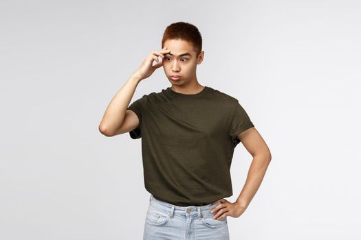Annoyed and distressed, tensed asian guy facepalm, sighing irritated, look away trying avoid eye contact in awkward moment, dont like person, strange person approaching, grey background