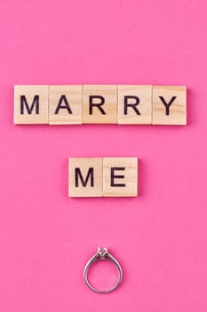 Flat lay top view of engagement ring and text marry me on wooden cubes.