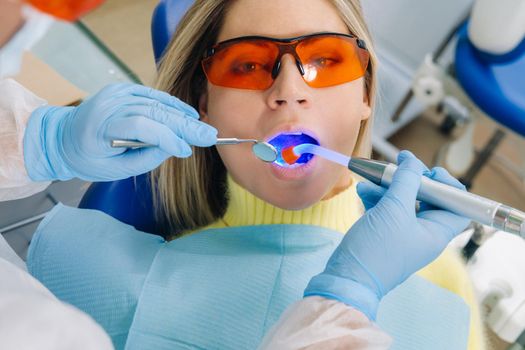 A young beautiful girl in dental glasses treats her teeth at the dentist with ultraviolet light. filling of teeth