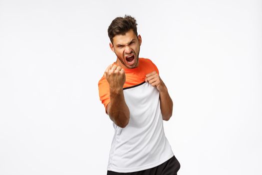 Sport, workout and active lifestyle concept. Agressive and focused handsome sportsman in sports t-shirt, clench fists, practice punches, shouting encouraged, showing boxing skills during exercise