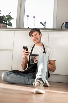 young man with glass of water reading SMS on his phone