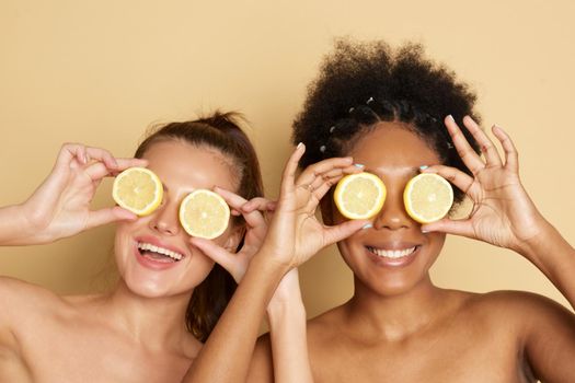 Colorful citrus circles near the face of cheerful multiracial women smiling and holding fresh citrus fruits near eyes while representing vitamin C benefits.