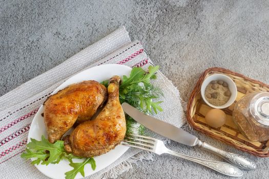On the table on a linen napkin is a plate with baked chicken legs and herbs. Next to the bread-spices. Top view, copy space