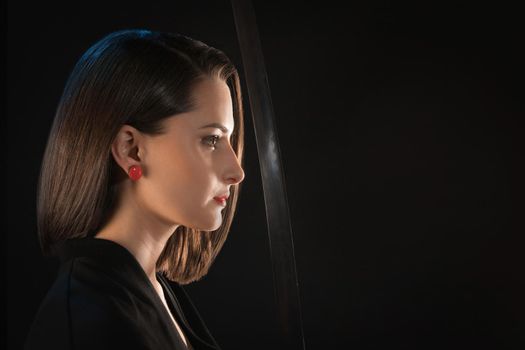 Portrait in profile of a young woman with red lips in front of a sharp blade of a saber on a black background