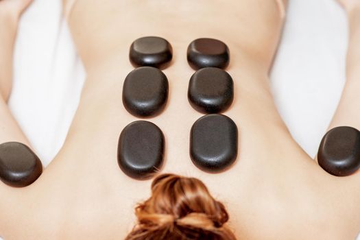 Black hot stones lying on female back