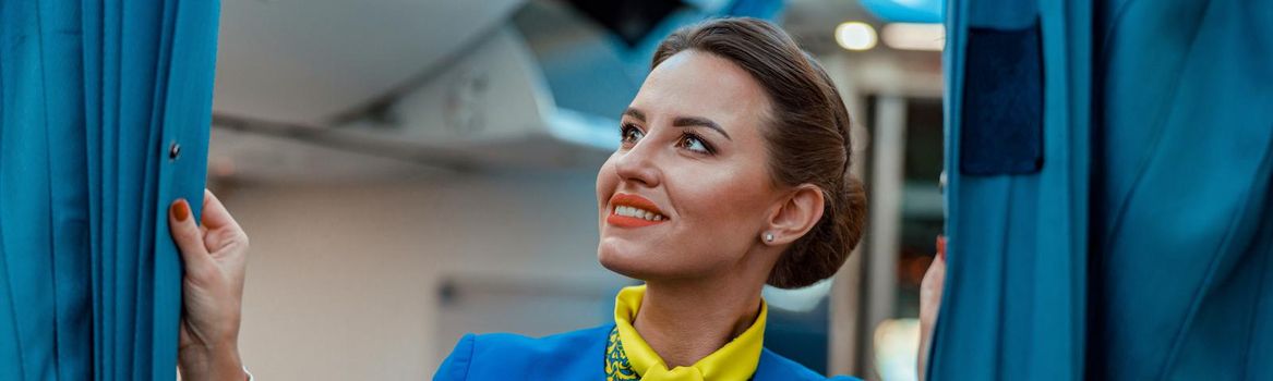 Cheerful woman stewardess holding curtains in airplane
