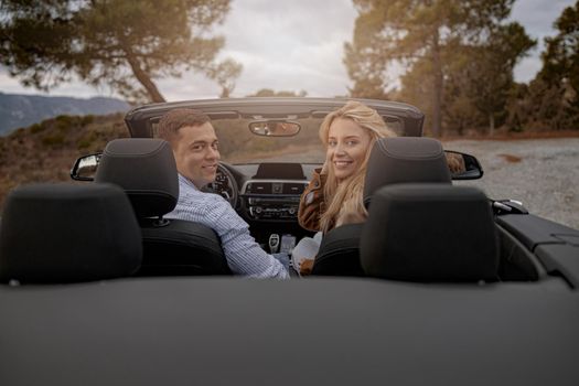 Happy couple of man and woman sitting in a convertible car and smiling while looking back