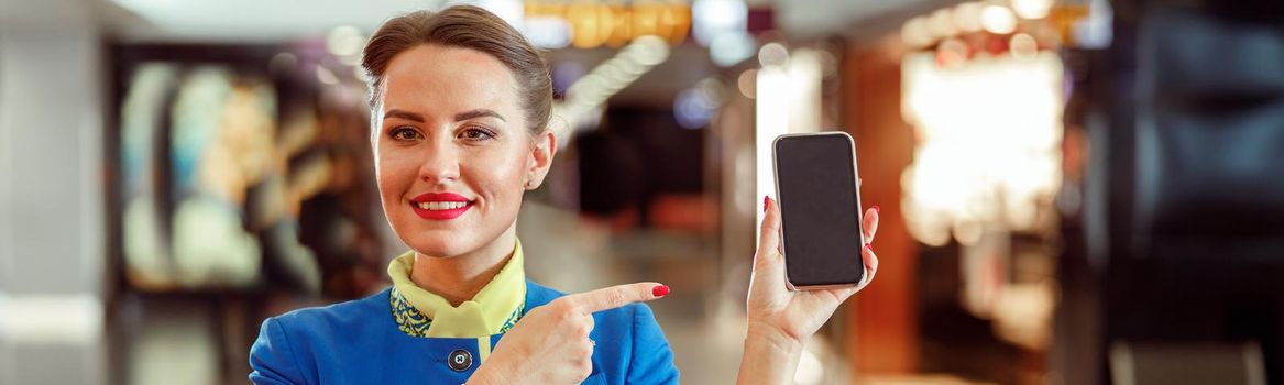 Joyful woman flight attendant pointing at smartphone at airport