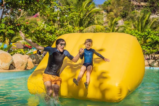 Dad and son go through an inflatable obstacle course in the pool