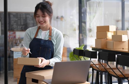 Shipping shopping online ,young start up small business owner writing address on cardboard box at workplace.small business entrepreneur SME or freelance asian woman working with box at home.