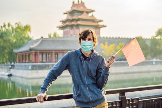 Enjoying vacation in China. Young man in medical mask with national chinese flag in Forbidden City. Travel to China concept. Tourists fear the 2019-ncov virus. Medical masked tourists