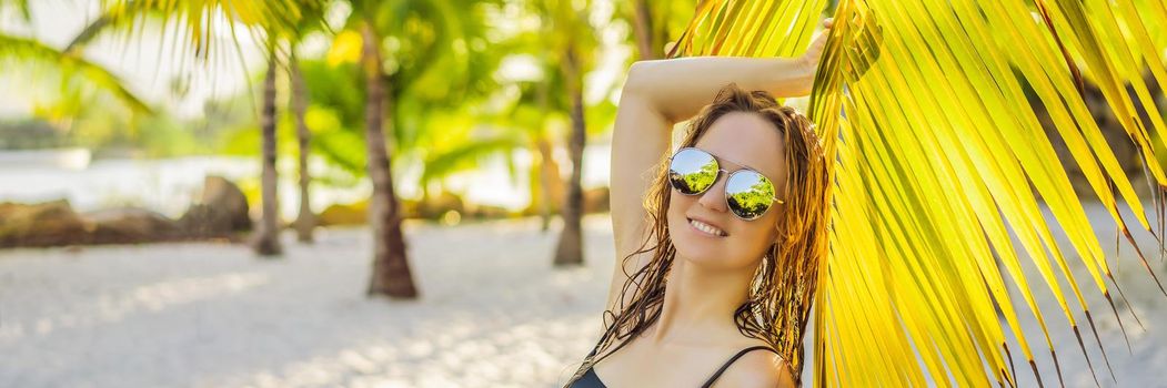 young beautiful woman in swimsuit on tropical beach, summer vacation, palm tree leaf, tanned skin, sand, smiling, happy. Happy traveller woman. BANNER, LONG FORMAT