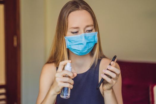 disinfection of the phone. A woman in a medical mask holds a telephone and a spray disinfector in her hands. protection of electronic devices from coronavirus transmission