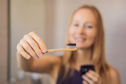 young woman brushing her teeth with a black tooth paste with active charcoal, and black tooth brush in her bathroom.