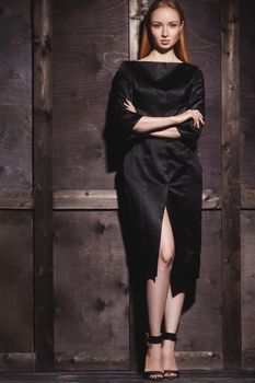 Fashion portrait of beautiful young woman in sexy black dress near with wood wall. Elegant dark evening look