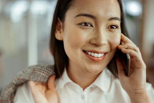 Close up of smiling asian business woman making phone call standing at office