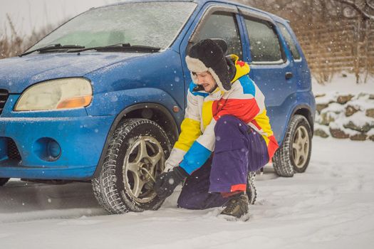 Winter accident on the road. A man changes a wheel during a snowfall. Winter problems