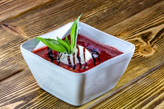 Tasty sweet dessert of ice cream poured with berry sirup in glass ramekin on wooden table. From above. Unfocused background