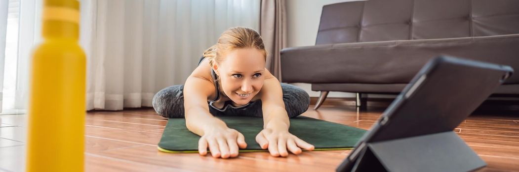Fitness woman exercising on the floor at home and watching fitness videos in a tablet. People do sports online because of the coronovirus BANNER, LONG FORMAT