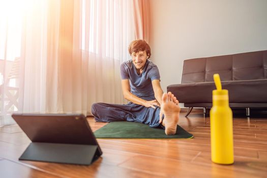 Fitness man exercising on the floor at home and watching fitness videos in a tablet. People do sports online because of the coronovirus