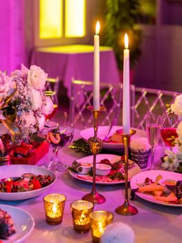 Table served for banquet or romantic date with candles and floral compositions. Beautiful decorations in pink electric light.