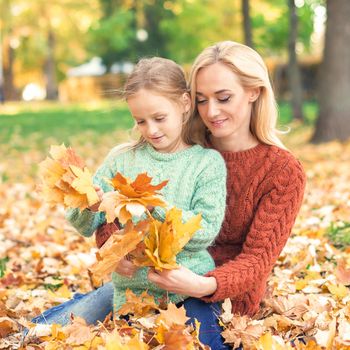 Woman and girl holding autumn yellow leaves