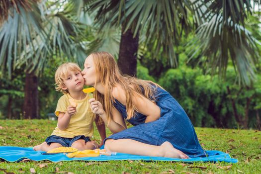 Coronavirus is over. Quarantine weakened. Take off the mask. Now you can go to public places. Mom and son had a picnic in the park. Eat healthy fruits - mango, pineapple and melon. Children eat healthy food
