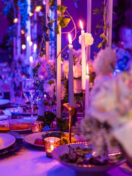 Table served for banquet with candles and floral compositions. Beautiful decorations in blue and purple electric light.