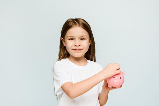 A little girl puts a coin in a piggy bank. The concept of teaching children personal finance and saving.